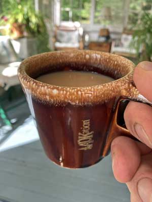 Individual holding mug of coffee with the text “ADKation” vertically near the handle for the user to see and recall memorable Adirondack vacation experiences. Part of Our ADKation Story and ADK vacation gift collection.
