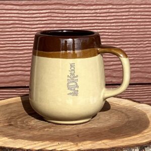 A two tone, old style ADK souvenir coffee mug with the text “ADKation” engraved vertically, reconnecting individuals to cherished Adirondack vacation emotions and moments.